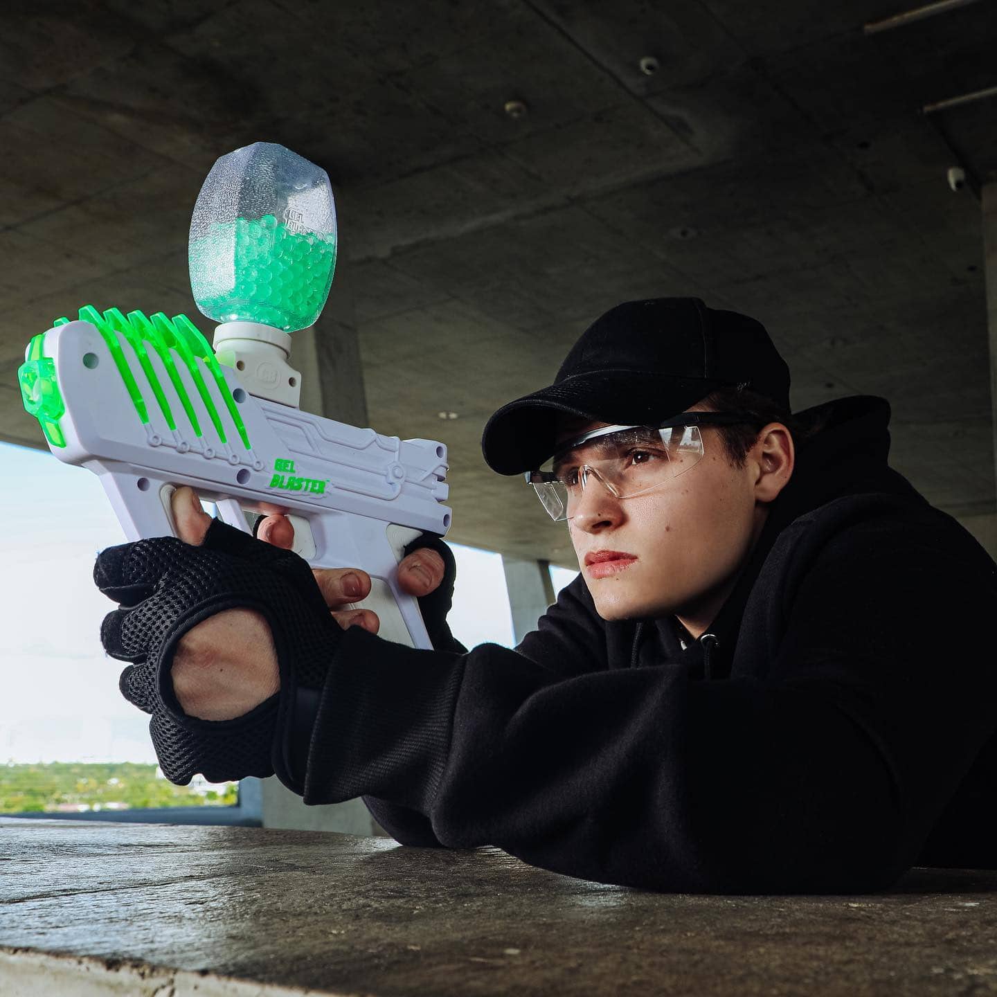 Igrač sa zaštitnim naočalama cilja bijelim Gel Blaster markerom punim zelenih gel kuglica