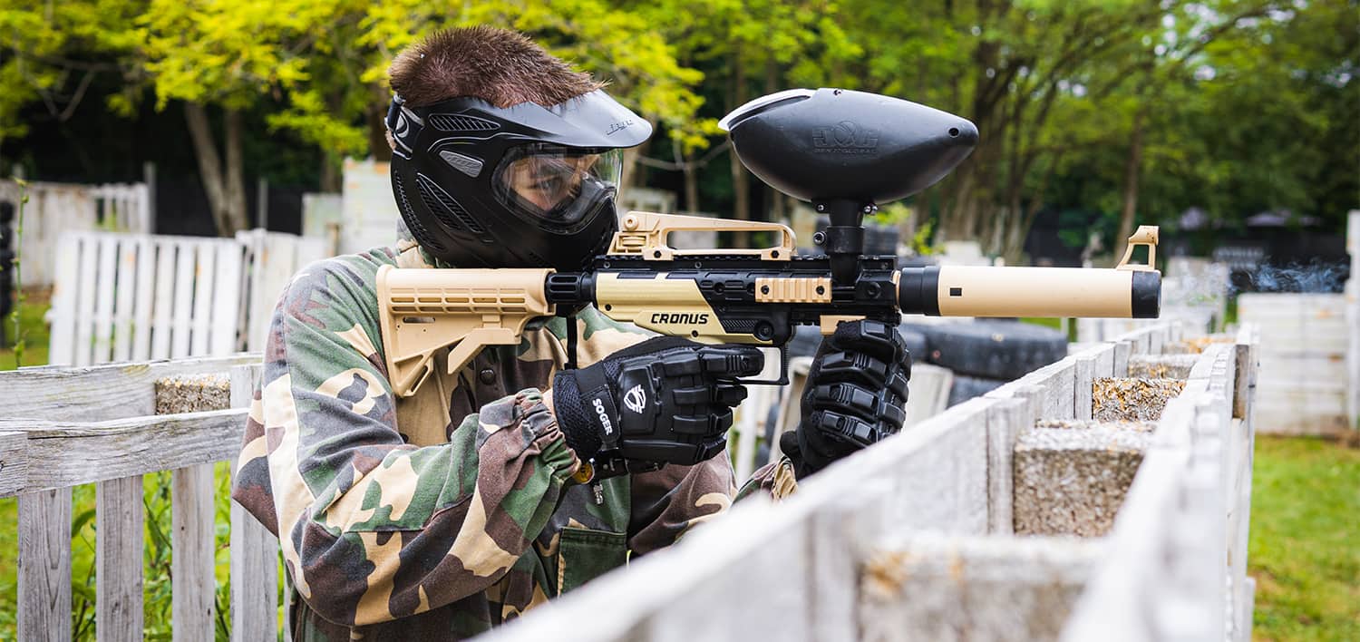 Igrač u kamuflaži cilja Tippmann Cronus markerom preko drvenog zaklona